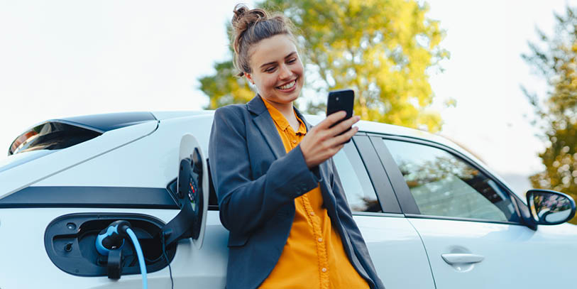 Frau lädt Elektroauto und steuert Ladevorgang mit Smartphone